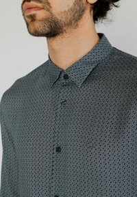 Camicia button-up con colletto stretto, caratterizzata da un motivo geometrico in blu scuro e bianco. Chiusura con bottoni e vestibilità regolare.