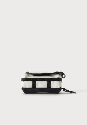 Pochette rectangulaire crème et noire avec fermeture éclair, sangles noires en sangle sur le devant et un clip noir sur le côté.