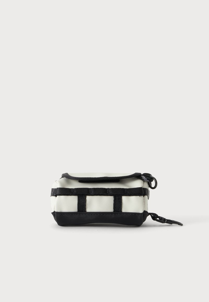 Pochette rectangulaire crème et noire avec fermeture éclair, sangles noires en sangle sur le devant et un clip noir sur le côté.