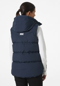 Gilet imbottito blu navy con cappuccio, caratterizzato da un design trapuntato, logo bianco sulla schiena e zip laterali. Texture liscia e tessuto resistente.