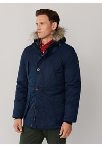 Chaqueta parka azul marino con tela aislante, capucha con forro de piel, cremalleras frontales y botones de presión, que cuenta con bolsillos laterales y textura acolchada.