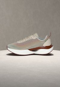 Αθλητικό παπούτσι ανοιχτό μπεζ με επάνω μέρος από πλέγμα με σχέδιο κυψέλης, καφέ λεπτομέρεια στη μέση της σόλας, λευκή σόλα και θηλιά έλξης σε ουδέτερο φόντο.
