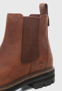 Hnědá kožená kotníková bota Chelsea s elastickou boční částí, texturovaným povrchem, táhlem na nazouvání a podrážkou s hrubým vzorkem. Obsahuje decentní ražbu loga na straně.