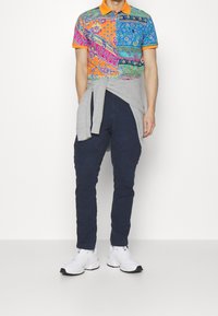 Färgglad polo med orange krage, blandade mönster i blått, rosa och grönt, kombinerad med marinblå cargobyxor och vita sneakers.