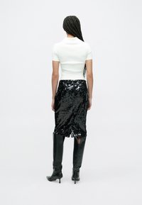 Top alb cu mâneci scurte, mulat, asortat cu o fustă midi neagră cu paiete și cu o despicătură laterală, purtată împreună cu cizme negre din piele până la genunchi.