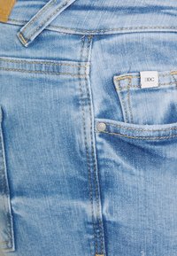 Ljust blå denimjeans har en klassisk design med synliga sömmar, en liten framficka och en märkesetikett på bakfickan.