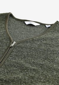 Green zip-up sweater with a V-neckline, made of textured material. Features a metal zipper and a simple tag inside.