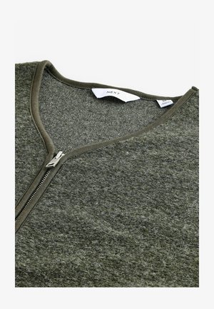 Roheline tõmblukuga kampsun V-kaelusega, valmistatud tekstureeritud materjalist. Omab metallist tõmbluku ja sisemiselt lihtsat sildi.