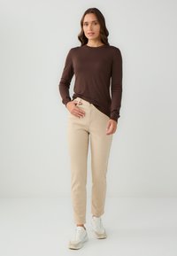 Bruine lange mouw top met een ronde hals, gecombineerd met beige aansluitende broek en witte sneakers. Eenvoudig ontwerp en zachte stoftexturen.