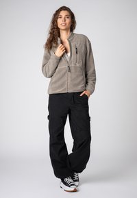 Hellgraue Fleecejacke mit durchgehendem Reißverschluss und linker Brusttasche. Kombiniert mit lockeren schwarzen Cargo-Hosen und weißen Sneakern.