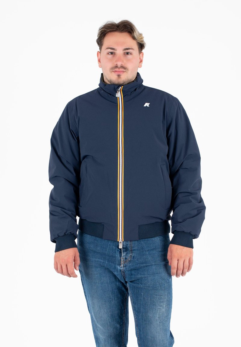 Giacca bomber blu navy con colletto alto, cerniera gialla e bianca, polsini e vita a costine. Presenta un piccolo logo sul petto.