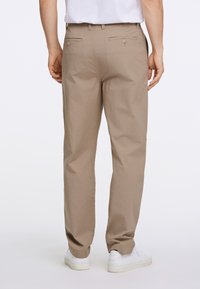 Beige broek van stof met een gladde textuur, voorzien van twee achterzakken en een relaxte pasvorm, gecombineerd met witte sneakers.