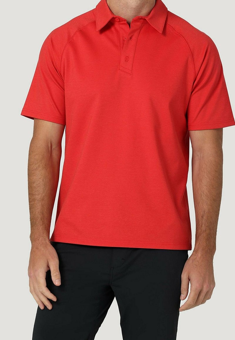 Homme portant un polo rouge uni à manches courtes avec des boutons, associé à un pantalon noir, visible du cou jusqu'à la mi-cuisse.