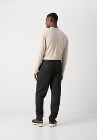 Chemise beige à manches longues, pantalon vert foncé et baskets noires avec des accents à motifs. L'ensemble présente une coupe décontractée et peu de détails.
