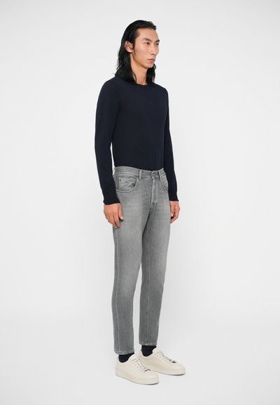 Μπλέ πουλόβερ με μακριά μανίκια, γκρι τζιν σε στενή εφαρμογή και λευκά αθλητικά παπούτσια. Απαλές υφές, άνετη εφαρμογή και ουδέτερη παλέτα χρωμάτων.