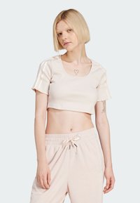 Světle růžový krátký top s žebrovanou texturou, s výstřihem do véčka a krátkými rukávy, který má kontrastní pruhy z látky podél ramen.