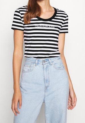 Femme portant un t-shirt Calvin Klein Jeans rayé noir et blanc rentré dans un jean en denim bleu clair taille haute.