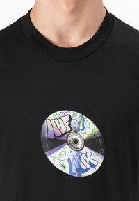 Black cotton T-shirt featuring a graphic print of a CD with the text "NUF 97" and "MIK," surrounded by colorful stars and doodles.