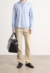 Ljusblå skjorta, beige byxor, svarta läderskor och en svart läderväska med handtag. Enkel design och välsittande silhuett.