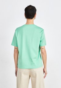 Camiseta verde menta de algodón, con cuello redondo y mangas cortas. Diseño sencillo con un corte relajado y sin patrones o acentos visibles.