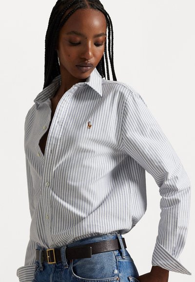 Camisa de botones a rayas con rayas verticales en azul y blanco, que presenta un pequeño logo bordado en el pecho y un cuello clásico.