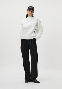 Sweat-shirt blanc avec des passepoils noirs et le logo "LeGer". Associé à un pantalon large noir et des bottines en cuir noires. Casquette noire portée à l'envers.