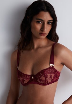 Soutien-gorge à armatures en dentelle bordeaux avec des panneaux transparents, des bretelles en satin réglables, un matériel décoratif en or et des détails floraux.