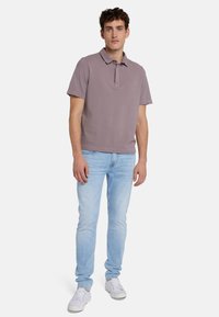 Polo grigio con colletto, maniche corte e orlo dritto, abbinato a jeans azzurri e sneaker bianchi. Design semplice e casual.