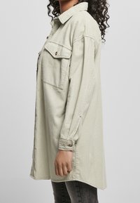 Ljusgrön kordflosshjorta med krage, två bröstfickor, långa ärmar och knäppta manschetter, med vertikal ribbad struktur.