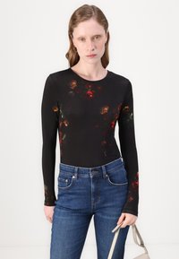 Body de manga larga negro con un patrón floral en rojo y amarillo, combinado con jeans de denim azul. El material parece suave y ajustado.