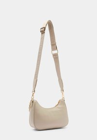 Borsa a tracolla in pelle beige con design curvo, tracolla regolabile con dettagli del logo e accenti in metallo color oro.
