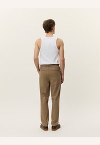 Camiseta sin mangas blanca para hombre y pantalones de vestir de cintura elástica de color marrón claro con bolsillos traseros, vistos desde atrás. Tejido suave y ligero.