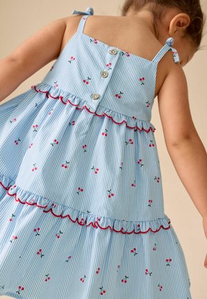 Toddler wearing blue and white striped dress with red cherry print, ruffled tiers, buttoned back, and tied shoulder straps.