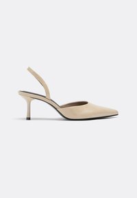 Chaussure à talon haut beige à bout pointu avec bride arrière, talon fin et semelle noire sur fond gris clair.