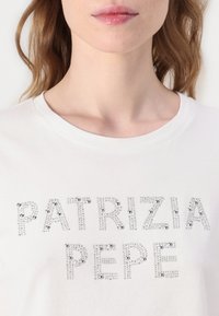 Hvit bomull t-skjorte med sølv rhinestone bokstaver som staver "PATRIZIA PEPE," rund hals, glatt tekstur og korte ermer.