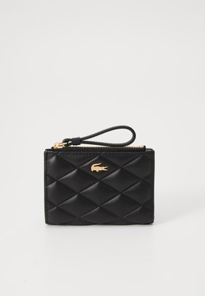 Black quilted wallet made of leather, featuring a gold zipper, wrist strap, and a gold logo accent on the front. Compact rectangular design.