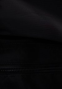 Tela negra con una textura suave, que presenta una cremallera horizontal a lo largo del borde inferior y un sutil patrón acanalado.