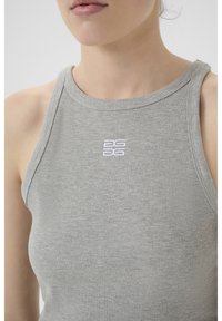 Pilkos juostos, be rankovių, maikutė. Išskirtinis baltas logotipas krūtinės srityje. Audinys atrodo švelnus ir prigludęs.