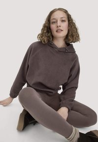 Donkerbruine fleece hoodie met een voorzak, trekkoord en een ontspannen pasvorm, gecombineerd met bijpassende leggings en zwarte enkellaarzen.