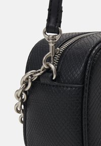 Borsa in pelle nera con texture, dotata di una zip argentata, dettaglio in catena e tracolla staccabile per opzioni di trasporto versatili.