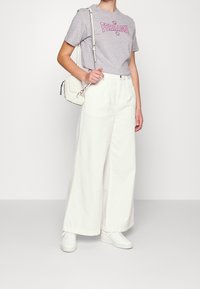 Camiseta de algodón gris con texto rosa "Ferragni", combinada con pantalones de mezclilla anchos blancos y zapatillas blancas. Pequeño bolso blanco cruzado.