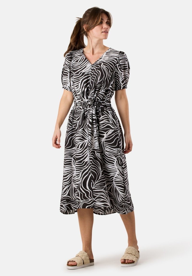 Schwarz-weißes Zebra-Print-Wickelkleid mit kurzen puffigen Ärmeln, tailliertem Schnitt und fließendem Rock. Kombiniert mit beigen Slipper-Sandalen.
