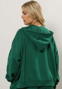 Felpa verde con cappuccio, dal taglio rilassato, caratterizzata da un cappuccio regolabile, maniche ampie e polsini e bordo a coste. Tessuto morbido.