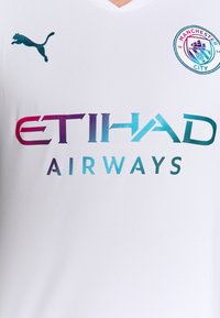 Bílý fotbalový dres s designem ve tvaru písmene V, strukturovanou tkaninou, tyrkysovým logem Puma a grafikou "ETIHAD AIRWAYS" v gradientních barvách.