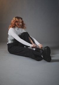 Baskets noires épaisses avec semelle texturée, associées à un pantalon noir ample et un gilet métallisé ajusté porté sur un col roulé blanc.