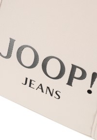 Beżowa torba materiałowa z napisem "JOOP! JEANS" w wyrazistych czarnych literach, posiadająca teksturowaną powierzchnię i minimalistyczny design.