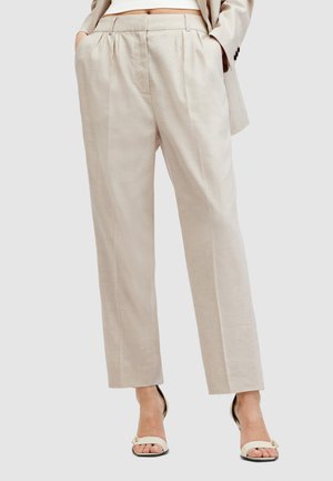 Lichtbeige linnen broek met een rechte snit, voorzien van plooien en zijzakken, gecombineerd met witte hakken.