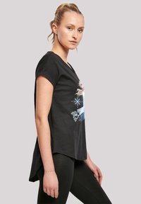 Svart bomull t-skjorte med korte ermer, med et fargerikt grafisk design av en karakter og snøfnugg på forsiden. Buet fald.