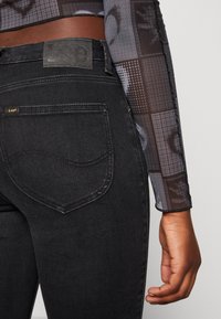 Svarta denimjeans med en texturerad tyg, med en sydd bakficka och en läderlogotyp på midjebandet.