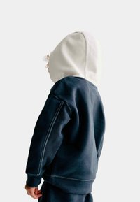 Marineblauwe sweatshirt met witte accenten. Beschikt over een contrasterende witte capuchon, textuur stof en geribbelde manchetten. Eenvoudig ontwerp, geen patronen.